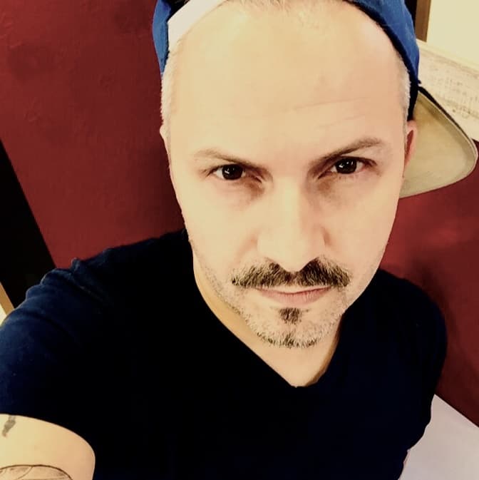 Roger Massimo in a cap, photographed against a red studio wall