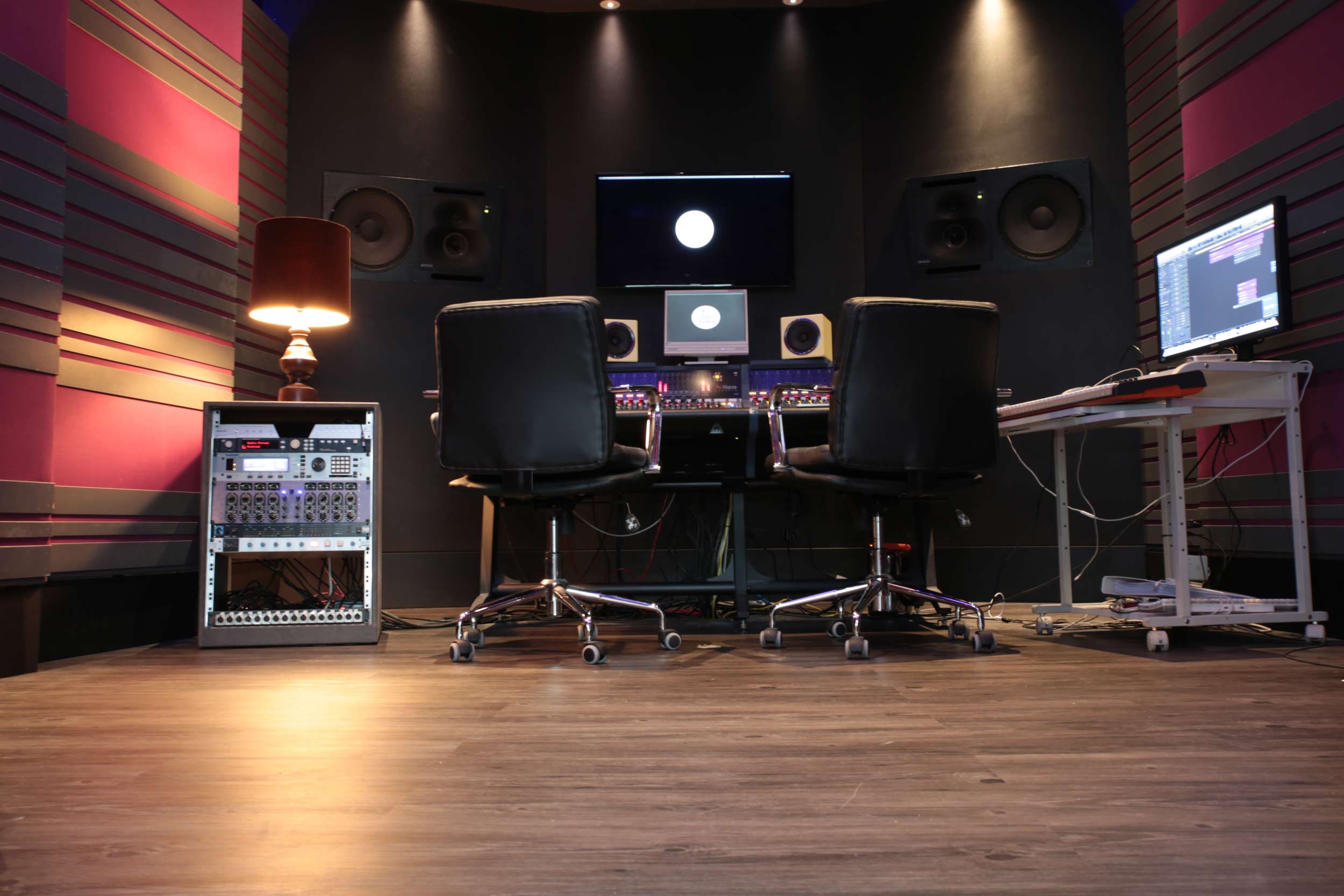 Low view across the Suite floor towards the console, with two chairs, an outboard rack and a warm table lamp