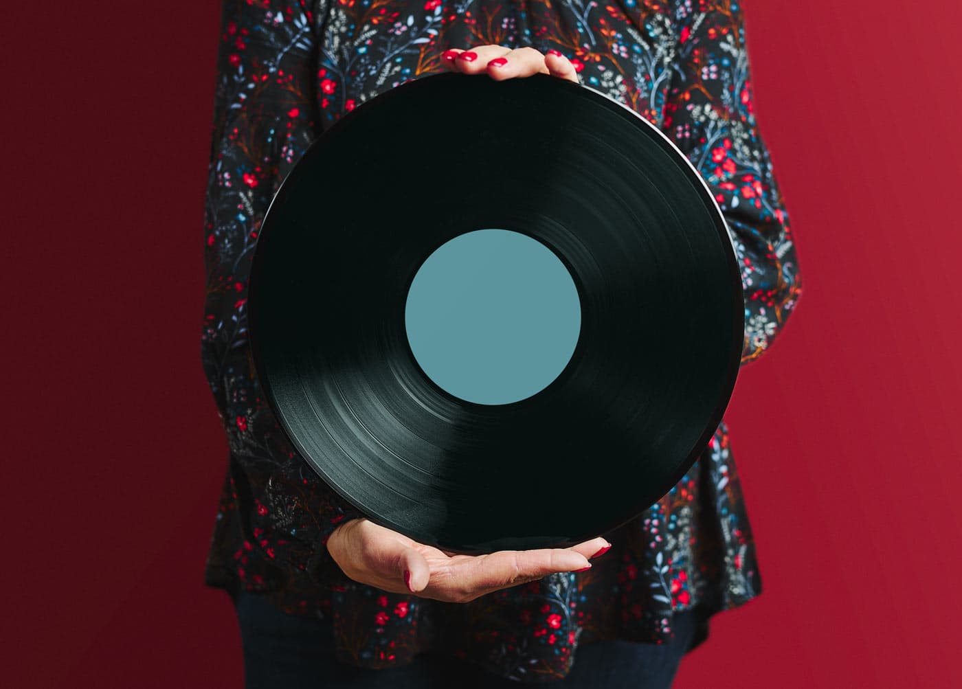 A vinyl record held up in both hands in front of a patterned dress